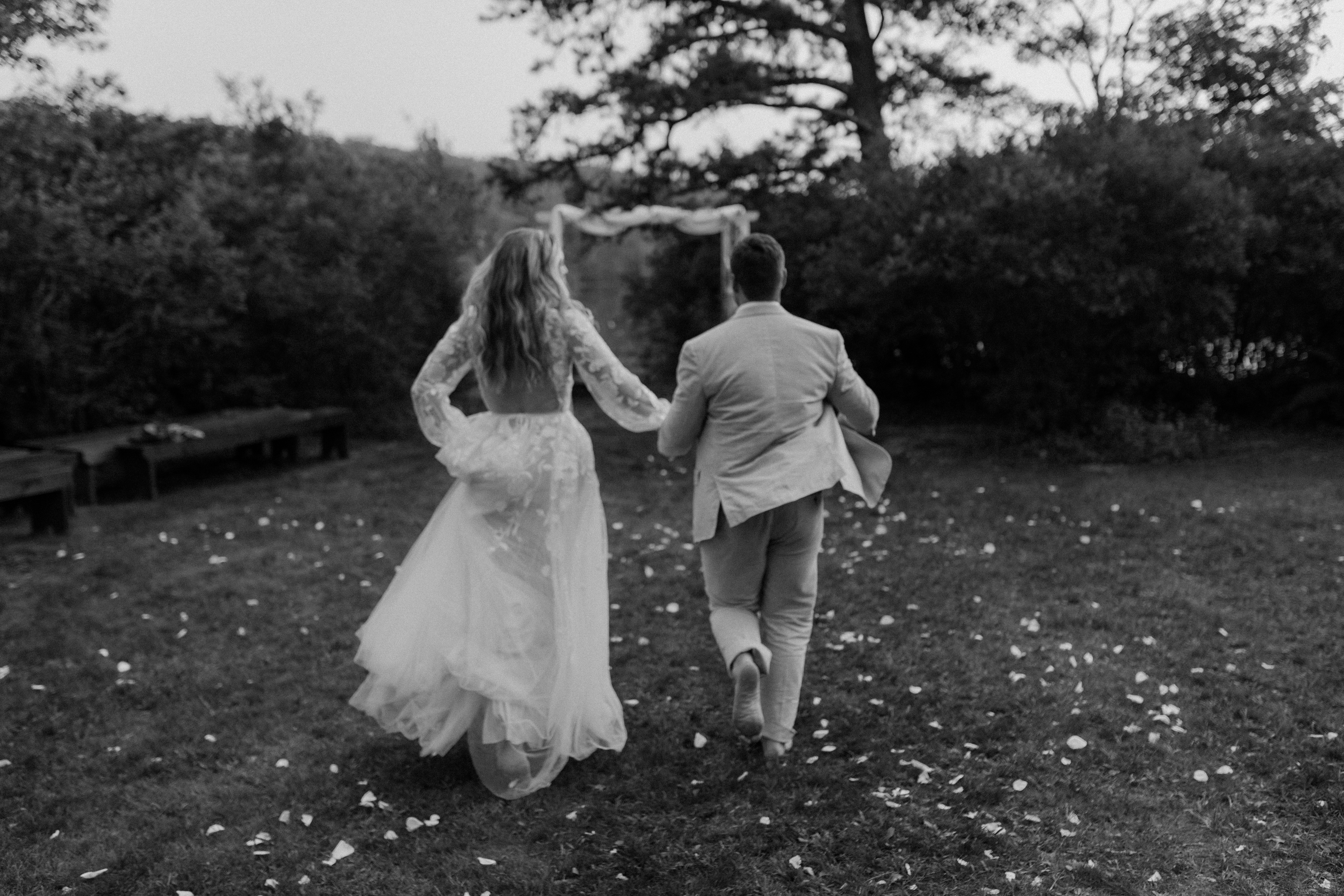 bride and groom running barefoot through grassy lawn